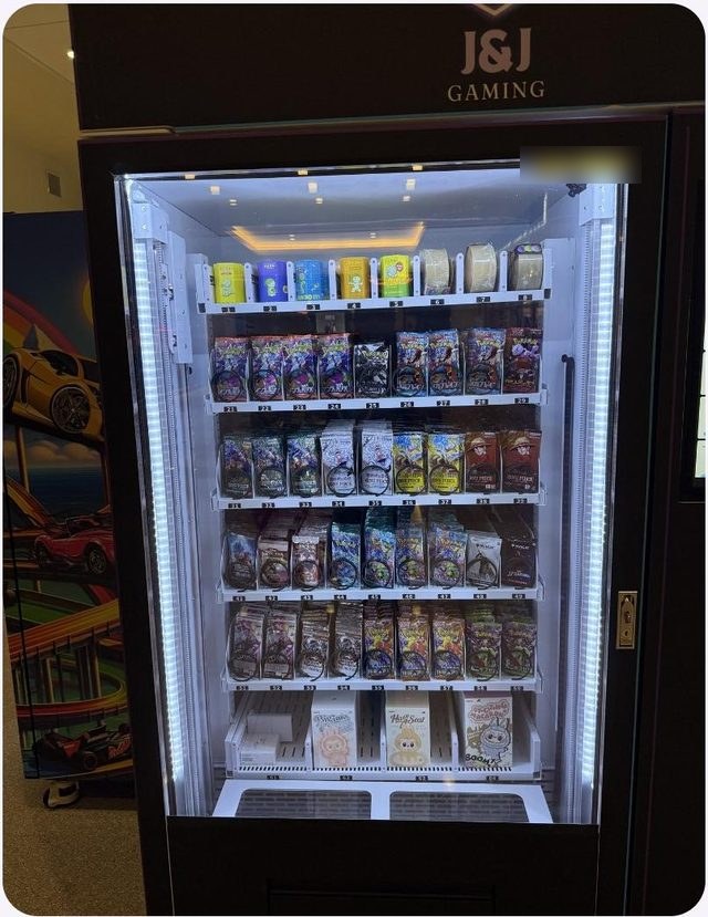J&J collectibles machine with lit glass shelves of sealed trading card packs and a touchscreen